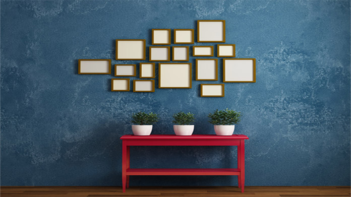 A variety of picture frames on a wall above a table with houseplants