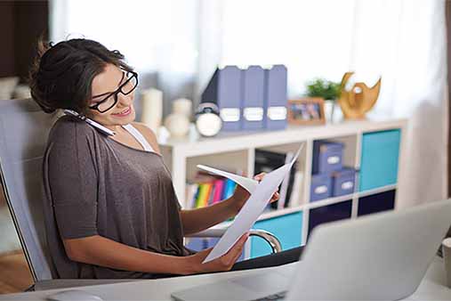 Smiling woman working at desk while on phone.