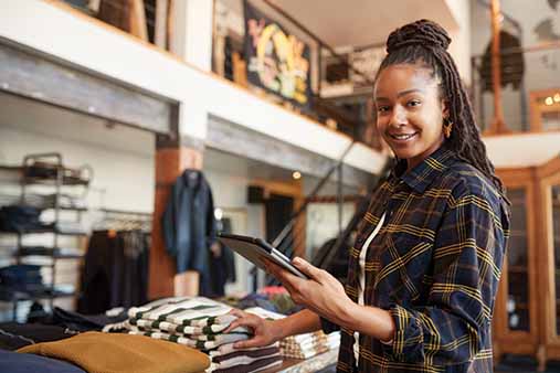 A woman standing in her clothing boutique taking inventory on her tablet.