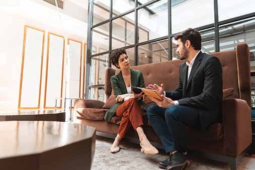 Man and woman sitting on a couch discussing business.