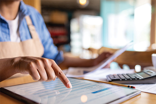 A woman is bookkeeping while using a calculator and a laptop.