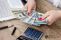 Woman Counting Money at her desk with a calculator and computer