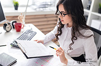 A businesswoman sits at a desk with a clipboard